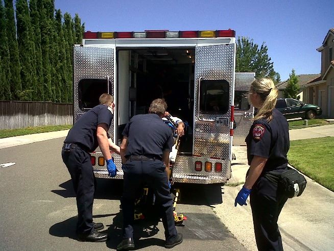 EMS workers lift someone on a stretcher into the back of an ambulance.