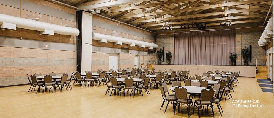 Image of large hall with hardwood floors, high ceilings, stage with curtains, and tables and chairs