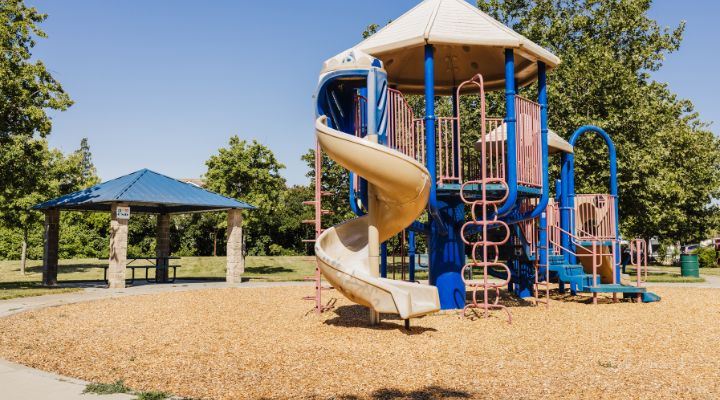 Left: picnic table under a blue shade structure. Right: a tan, blue, and red playground 
