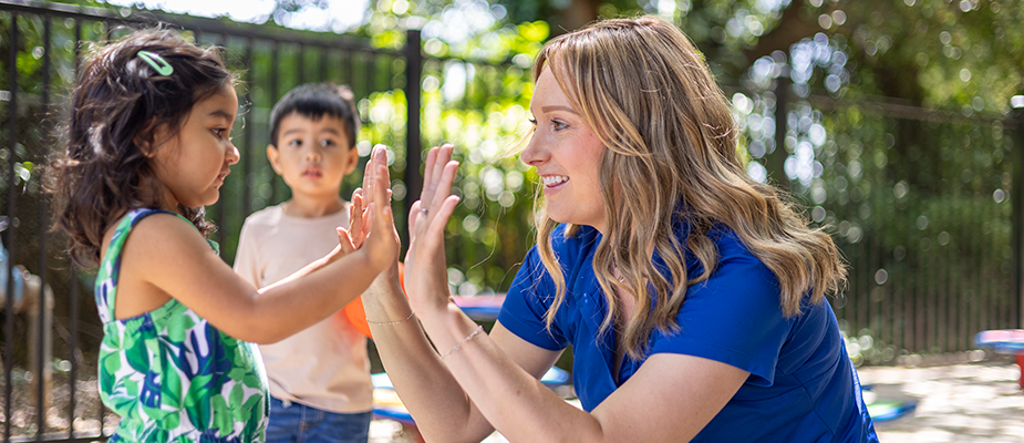 A teacher and a preschool girl high five.