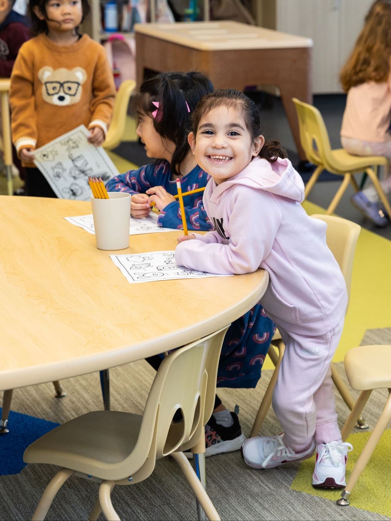 A preschool calss hugs their teacher.