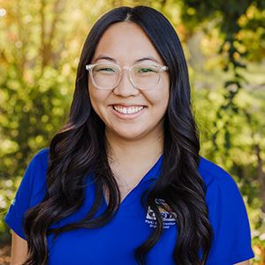 A dark-haired woman wearing glasses smiles.