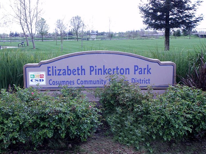 Pinkerton Park Sign with green shrubs and a dark cloudy sky