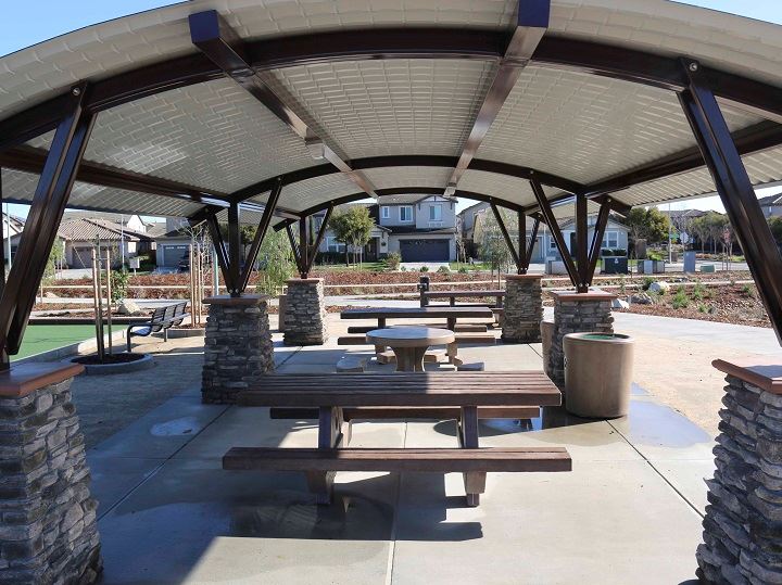 Arching picnic cover in white with brown beams and cement picnic tables underneath