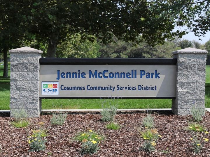 Jennie McConnell Park sign between 2 stone columns with tress in the background