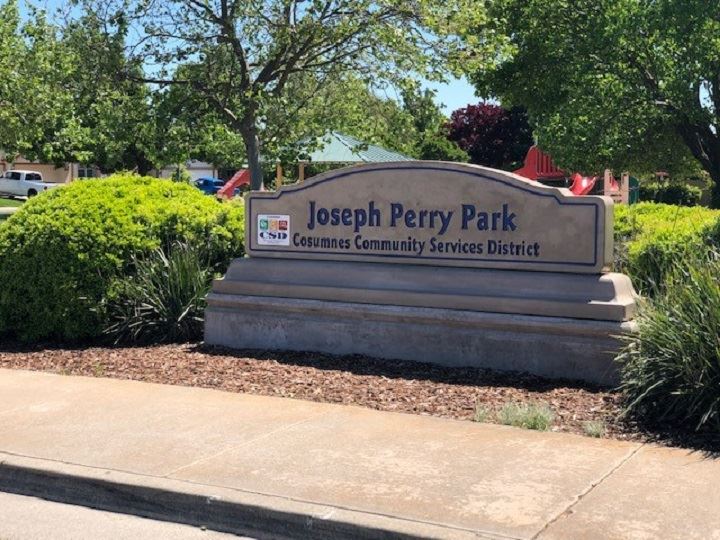 Monument style park sign with green shrubs and trees